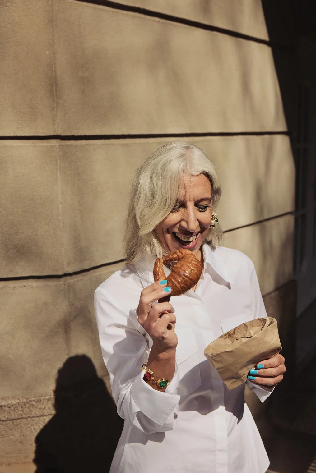 Woman smiling and eating a croissant outdoors in warm sunlight