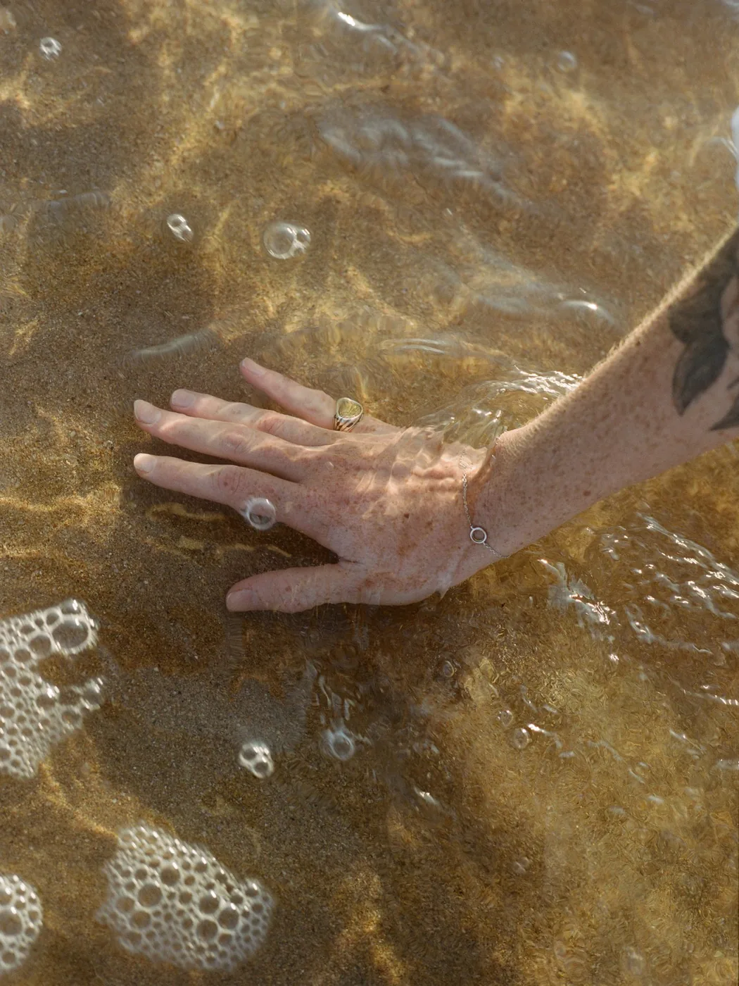 Close-up of a hand touching sunlit, sandy water, bubbles and light rippling across the surface