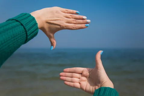 Hands framing the horizon against the sky and sea